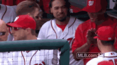 a group of baseball players are standing in a dugout talking to each other .
