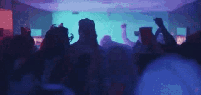 a crowd of people are dancing at a party in a dark room with blue lights .