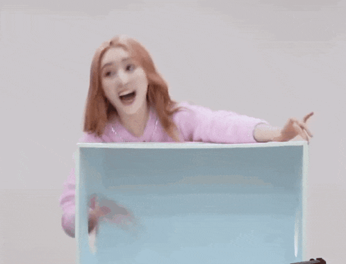 a woman in a pink sweater is standing behind a blue box .