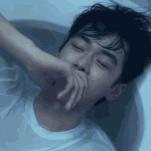 a young man is laying in a bathtub with his hand on his face