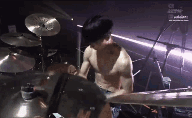 a shirtless man is playing drums in a band .