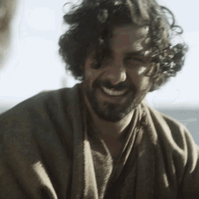 a man with curly hair and a beard smiles at the camera