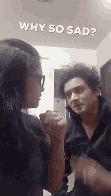 a man and a woman are standing next to each other and the woman is asking the man why he is so sad .