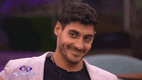 a man is smiling in front of a sign that says #grandefratello on it