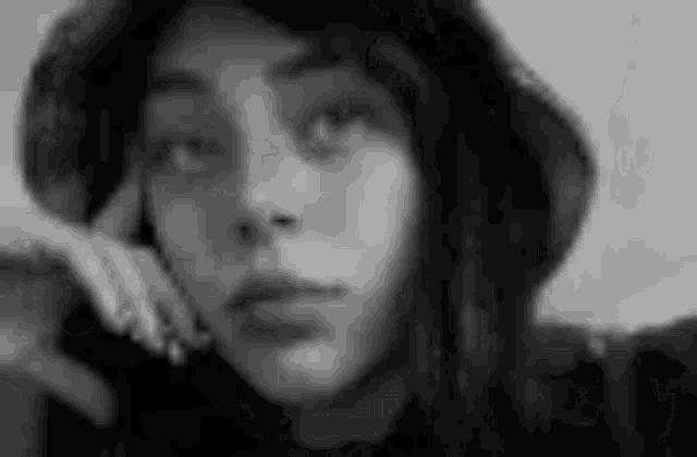 a black and white photo of a woman wearing a hat with her hand on her face .