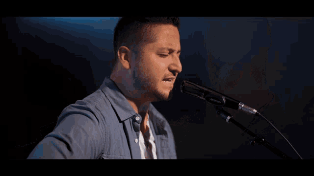 a man singing into a microphone with a guitar in the background