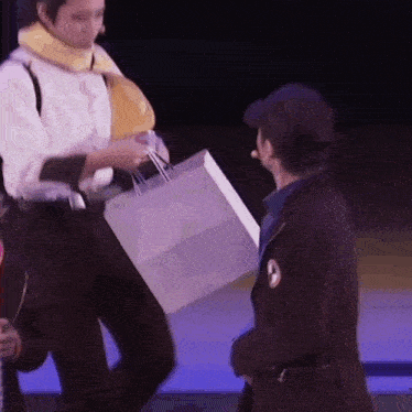a man is holding a shopping bag while standing next to another man on a stage .