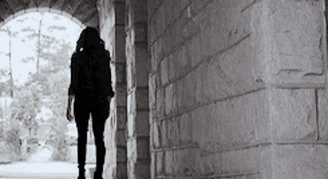 a woman is walking through a stone tunnel .