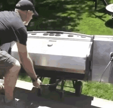a man in a black hat is pushing a cart with a grill in the background