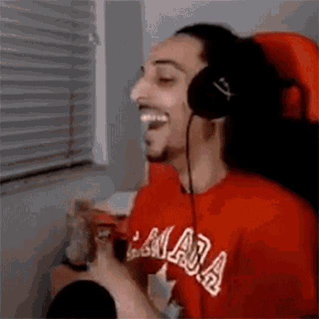 a man wearing headphones and a red shirt is sitting in front of a window .