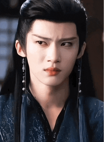 a close up of a man 's face with long black hair and earrings