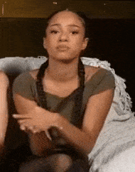 a woman is sitting on a bed with her arms crossed and making a face .