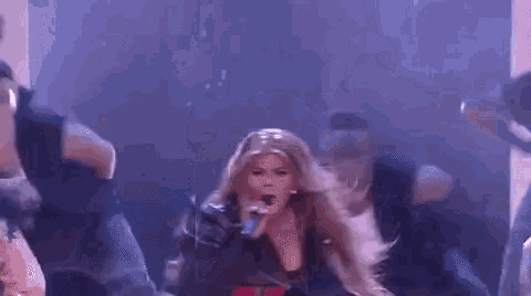 a woman is singing into a microphone while a group of dancers are dancing around her on a stage .