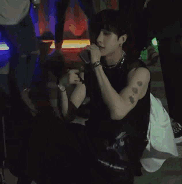 a man with a tattoo on his arm is kneeling down and talking into a microphone
