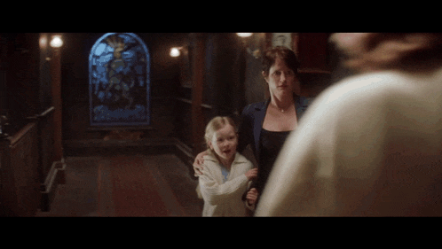 a woman and a little girl are in a hallway with a stained glass window in the background
