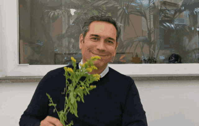 a man in a black sweater holds a bunch of yellow flowers in front of a window