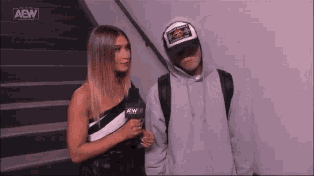 a woman is standing next to a man wearing a hoodie and a hat .