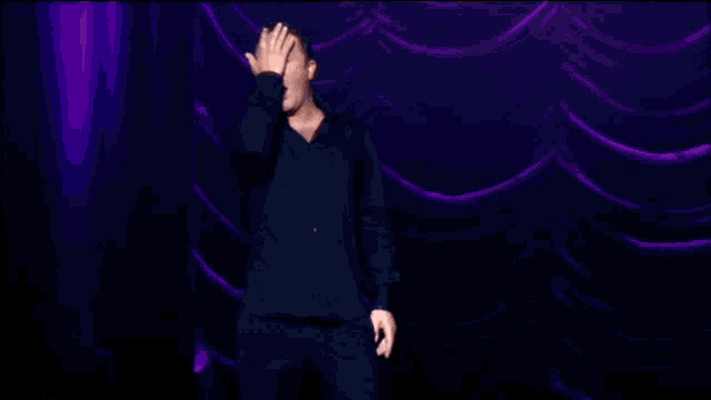 a man in a black shirt is standing on a stage with purple curtains behind him .