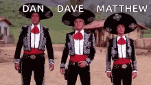 three men in mariachi costumes are standing next to each other on a dirt road holding guns .