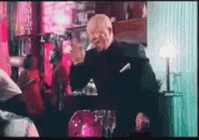a man in a suit is standing in front of a table with a glass of wine .