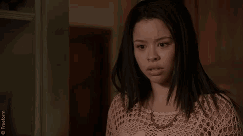 a girl in a crocheted top is standing in front of a door with a freeform logo on the bottom right