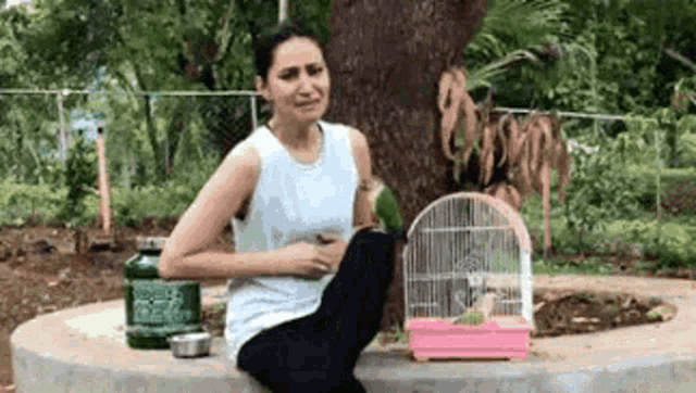 a woman is sitting on a bench holding her stomach while holding a bird in a cage .