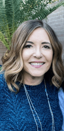 a woman in a blue sweater and necklace smiles for the camera