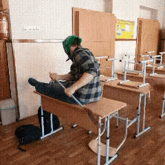a man wearing a green bandana sits on a desk in a classroom