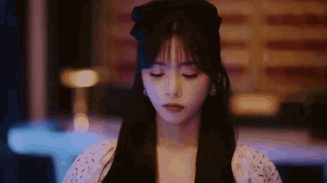 a woman with long black hair and a bow in her hair is looking down .
