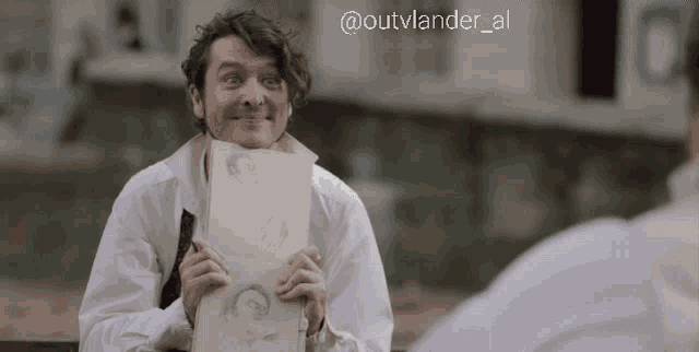 a man in a white shirt is holding a piece of paper in front of his face with a caption that says @outvlander_al
