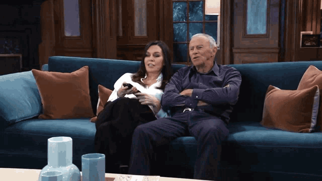a man and a woman are sitting on a blue couch watching television