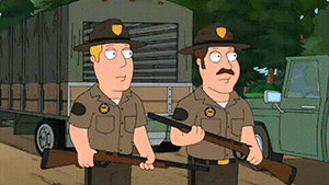 two park rangers are standing next to each other holding guns in front of a truck