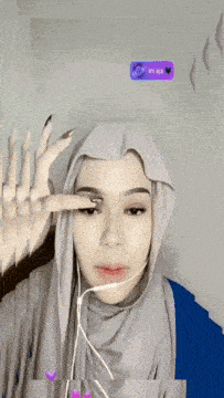 a woman wearing a hijab and ear buds has a purple i 'm aya sticker on her wall