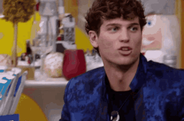 a man with curly hair is wearing a blue jacket and a black shirt
