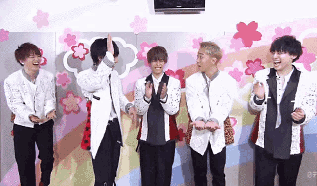 a group of young men are standing in front of a wall with pink flowers