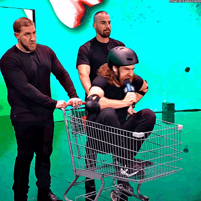 a man wearing a helmet is sitting in a shopping cart being pushed by two other men