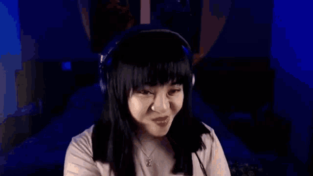 a woman wearing headphones is covering her face with her hands in a dark room .