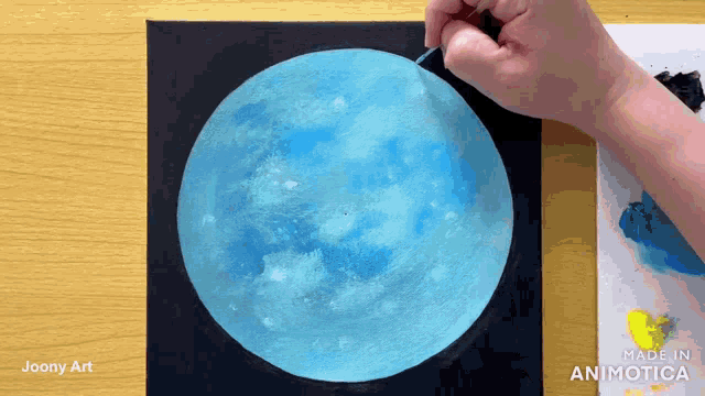 a person is painting a blue moon on a black canvas