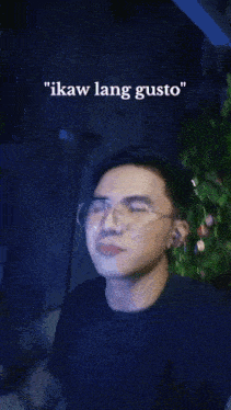 a man wearing glasses and ear buds says " ikaw lang gusto " in front of a christmas tree .