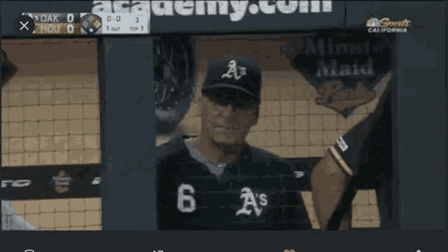 a baseball player wearing a black a's jersey stands in the dugout