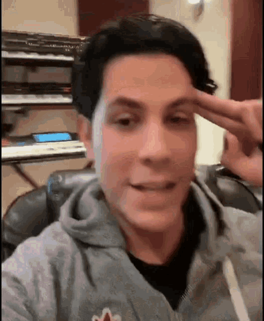 a man in a gray hoodie is making a peace sign with his finger .