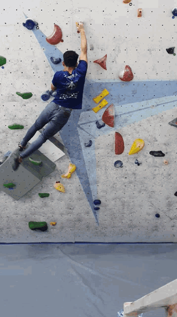 a man wearing a blue shirt that says ' sds ' on it is climbing a climbing wall