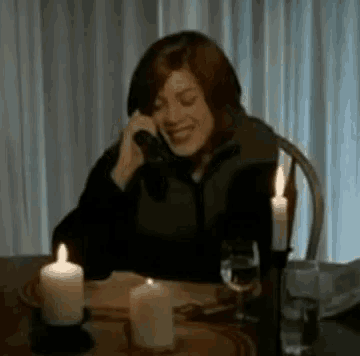 a woman is sitting at a table with candles and talking on a phone