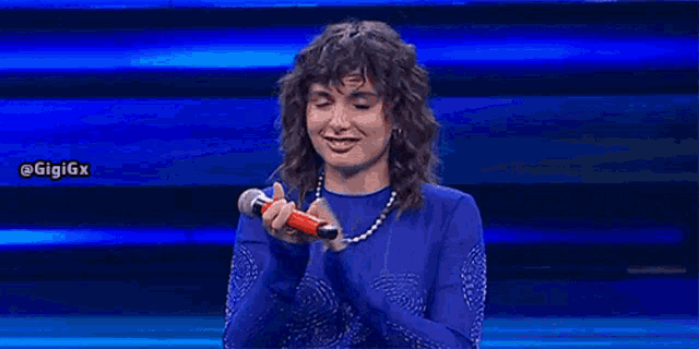 a woman in a blue top is holding a red microphone and smiling .