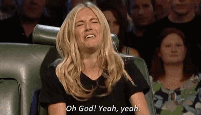 a woman is sitting in a chair with her eyes closed and laughing in front of a crowd .