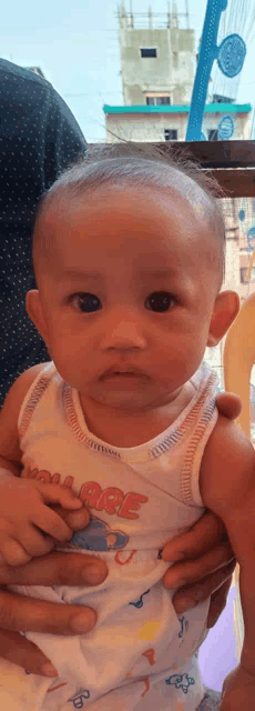 a baby is being held by a person wearing a tank top that says age on it