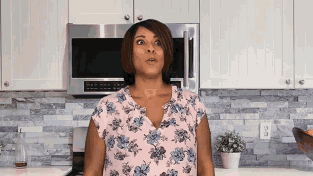 a woman in a floral shirt is standing in a kitchen