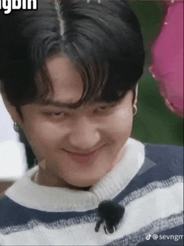 a young man wearing a striped sweater is smiling with a pink balloon in the background