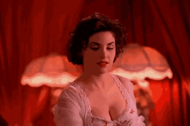 a woman in a white dress is standing in front of a lamp in a room with a red curtain .