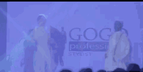 two men in white robes are dancing on a stage in front of a purple background .